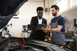 © sofiko14 - Mechanic wearing overalls discussing car repair details with businessman using digital tablet in workshop. Collaboration, technology, and automobile service concept.