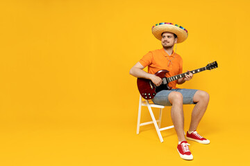 Wall Mural - Attractive young guy playing guitar in mexican hat