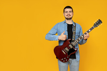 Wall Mural - Attractive young guy with a guitar in his hands on a yellow background