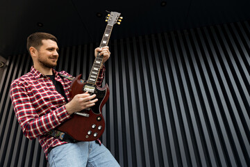 Wall Mural - A stylish young guy plays the guitar on a dark background