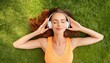 © Marko - Top view of beautiful young woman closed the eyes lying on short grass and listening music with headphone