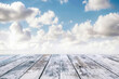 © oksa_studio - Wooden table top with empty space, with a blurred blue sky and clouds in the background, perfect for showcasing products