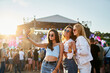 © artiemedvedev - Group of happy young women friends take selfie at sunny beach music fest. Girls in trendy summer outfits enjoy live concert, party atmosphere. Youth culture, friendship, outdoor entertainment moment.