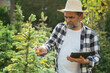 © standret - Black digital tablet in hand. Senior gardener is at work at daytime