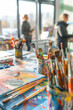 © Anna - Diverse paintbrushes and art supplies on a messy table in a bright, sunlit art studio. Art classes, creativity, art education, painting workshops, inspiration, artistic tools, creative environment.