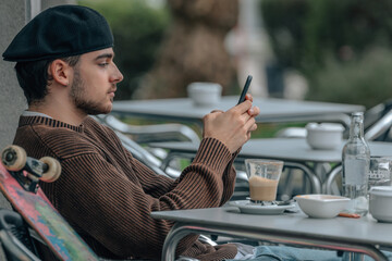 Canvas Print - young urban man on the cafe terrace with mobile phone and skateboard