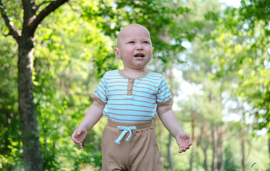 Baby crying in park in sunny summer park. Child experiences emotional excitement, disappointment, and annoyance. Portrait of human emotions. Advertising of children's products.