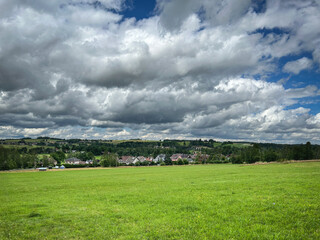 Wall Mural - Summer landscape with green meadow and small village under blue sky with white clouds