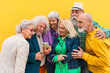 © Westend61 - Cheerful elderly woman sharing smart phone with friends in front of wall