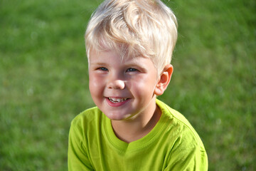 close up portrait of positive smiling blond boy on natural grass background.