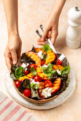 Wall Mural - Girl hands Serving summer peach caprese salad with tomatoes, basil, burrata cheese and balsamic sauce.