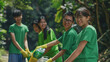 © VK Studio - A group of smiling young volunteers in green t-shirts work together outdoors, enthusiastically handling recycling materials and showcasing teamwork in a lush, green environment.