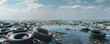 © wolfhound911 - A polluted ocean with a variety of garbage including old tires and plastic bags, highlighting the extent of pollution. The sky above is clear for copy space.