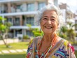 © Bijac - joyful elderly latina woman in a sunlit garden of a modern senior living community warm smile silver hair and colorful traditional clothing contrast with contemporary architecture