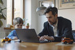 © Running opossum - Businessman is working from home at his laptop while his son is playing next to him