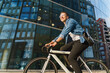 © muse studio - A joyful young man riding a bicycle past a modern glass building, exemplifying an energetic urban lifestyle.
