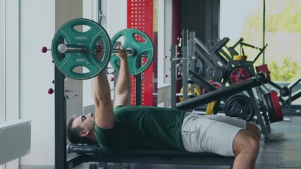 Wall Mural - Strong man lifting barbell, lying on sport bench at gym interior, side view, slow motion