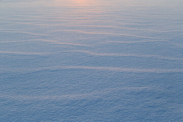 Landscape of fresh and clean snow on the ground at sunset. Good as a natural winter season background with copy space. Beautiful abstract snowy shapes.