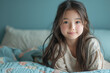© kora studio - cute asian girl in the white shirt sitting on the bed  in front of the blue background