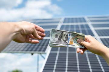 Wall Mural - Business man handing over dollar money to another hand against solar panel