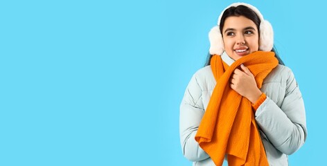 Wall Mural - Young woman in winter clothes on light blue background with space for text