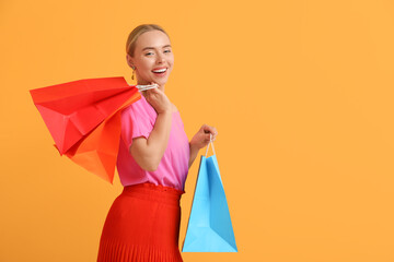 Poster - Happy young woman with shopping bags on orange background