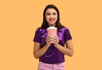 Poster - Beautiful young happy woman with bucket of popcorn on yellow background