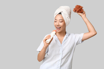 Poster - Young Asian woman with shower gel and loofah singing on light background