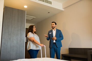 Handsome hotel manager showing room amenities to a tourist woman arriving with a suitcase