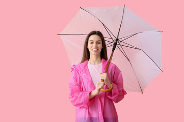 Wall Mural - Young happy woman in raincoat with opened umbrella on pink background