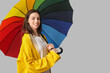 © Pixel-Shot - Young happy woman in raincoat with opened colorful umbrella on grey background