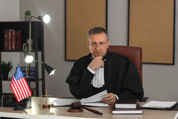 Wall Mural - Mature judge working with case file at table in dark office