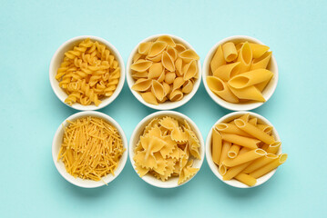 Wall Mural - Bowls with different tasty uncooked pasta on blue background