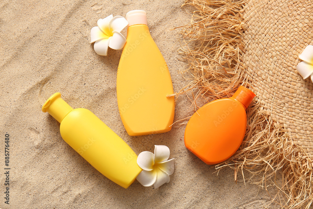 Bottles of sunscreen cream and flowers on sand