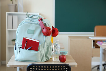 Wall Mural - Backpack with headphones, water bottle and apple on desk in classroom