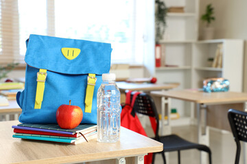 Wall Mural - Blue backpack with apple, copybooks and water bottle on desk in classroom