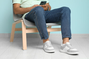 Wall Mural - Young man in stylish sneakers sitting on chair near blue wall, closeup