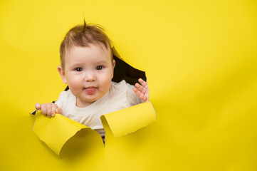 Cute Caucasian baby sticking out of a hole in a paper yellow background. 