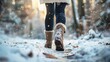 © tashechka - A person wearing winter boots walks through a snowy forest path, with snowflakes falling around them.