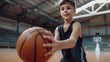 © Jiraphat - A young boy wearing a black basketball jersey practices dribbling a basketball indoors