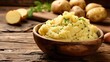 © Vodkaz - A bowl of creamy mashed potatoes garnished with chives, set on a rustic wooden table with whole potatoes in the background