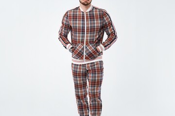 man wearing plaid tracksuit standing against white background.