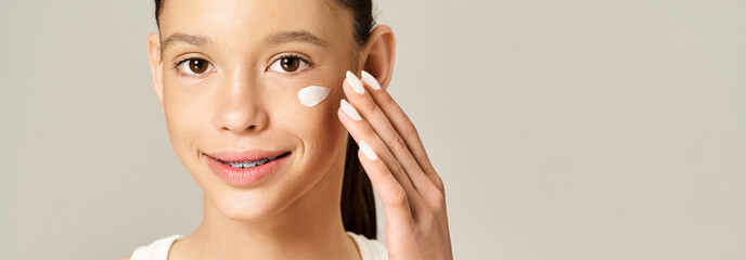 Wall Mural - A stylish teenage girl with vibrant attire applies cream on her face for a healthy, glowing complexion.