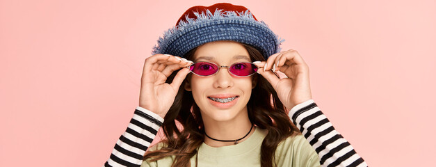 A stylish teenage girl poses confidently in vibrant attire, sporting a trendy hat and sunglasses.