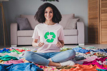 Sticker - Full length portrait of young girl sit pile stack clothes hold recycle donation card flat indoors