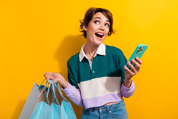 Sticker - Photo of cute excited lady dressed polo shirt rising shoppers texting modern device looking empty space isolated yellow color background