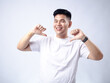 © Daniel - A young Asian man, wearing a white shirt and black watch, smiles confidently while pointing both thumbs at himself. The plain white background emphasizes the subject's self-assured