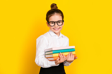 Poster - Photo of cute schoolgirl hold pile stack book wear uniform isolated on yellow color background