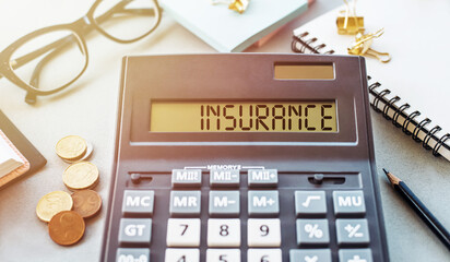 Wall Mural - A Calculator Displaying the Word Insurance on a Desk With Coins and Office Supplies