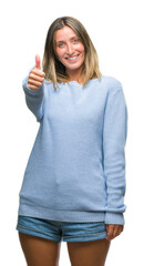 Young beautiful woman wearing winter sweater over isolated background doing happy thumbs up gesture with hand. Approving expression looking at the camera with showing success.